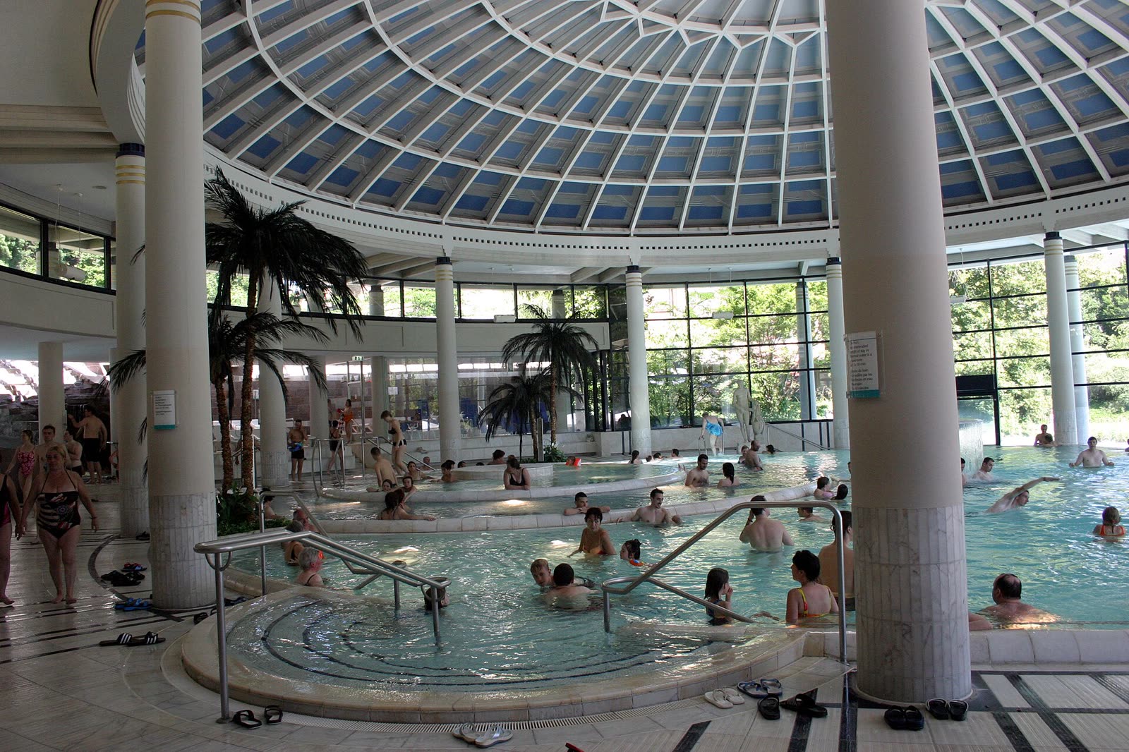 Bright domed thermal pool hall with palms and pale tile at Caracalla Therme in Baden-Baden.